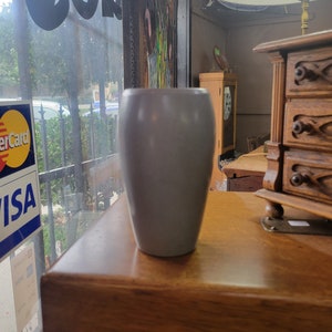 May include: A gray ceramic vase with a rounded bottom and a wide opening. The vase is sitting on a wooden table.