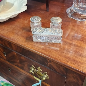 May include: A set of three antique silver-plated glass containers with intricate etched designs. The containers are arranged on a wooden surface with a drawer below.