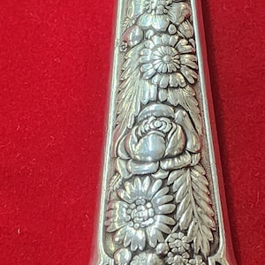 May include: A silver handle with an ornate floral design. The handle is detailed with leaves, flowers, and a rose.