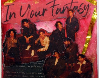May include: A square, resin-coated artwork featuring a group of people. The background is a vibrant pink with the words "In Your Fantasy" in black script. The image includes a collage of people in various outfits. Gold foil accents the edges.