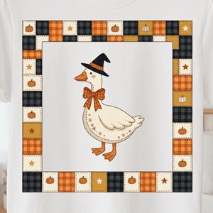 Puede incluir: Una camiseta blanca con un gráfico central de un ganso que lleva un sombrero de bruja negro y una pajarita de cuadros naranjas. El ganso está rodeado por un borde cuadrado compuesto por un patrón de parches de cuadros naranjas, negros y dorados.