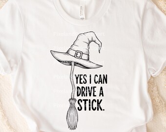 May include: White t-shirt featuring a black and white witch hat and broom graphic. The text "YES I CAN DRIVE A STICK" is printed below the hat. The shirt is made of a soft material.