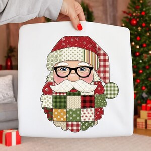 May include: A white square pillow featuring a patchwork Santa Claus design. The Santa has a white beard and mustache, black glasses, and a red and green patchwork hat and coat. The pillow is held by a person.