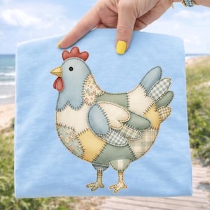 Könnte beinhalten: Ein hellblaues Stoffstück mit einem Patchwork-Hühnerdesign. Das Huhn hat einen roten Kamm und Kehllappen, einen gelben Schnabel und besteht aus verschiedenen Stoffmustern in Blau, Gelb und Blumenmustern. Der Artikel wird von einer Person gehalten.
