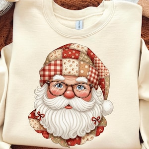 May include: Cream-coloured sweatshirt with a Santa Claus graphic. Santa is shown wearing glasses, a white beard, and a patchwork hat and collar in red, white, and tan. The design is festive and suitable for the holiday season.