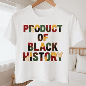 May include: White crop top with the text "PRODUCT OF BLACK HISTORY" in colorful patchwork letters. The letters are in shades of red, brown, yellow, and green. The shirt is hanging on a wooden hanger.