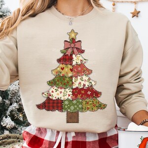 Puede incluir: Sudadera beige con un diseño de árbol de Navidad de patchwork. El árbol tiene un lazo rosa, una estrella dorada y varias secciones estampadas en rojo, verde y blanco. La sudadera es de manga larga y tiene cuello redondo.