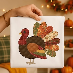 Könnte beinhalten: Ein weißes quadratisches Kissen mit einem bunten Truthahndesign. Der Truthahn hat einen braunen Körper, einen roten Wamm und Kopf sowie einen Fächer aus gemusterten Federn in Orange-, Grün- und Cremetönen. Das Kissen wird von einer Hand gehalten.