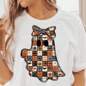 Könnte beinhalten: Weißes T-Shirt mit einem Patchwork-Geisterdesign und einer Schleife. Der Geist besteht aus Quadraten mit Halloween-Mustern, darunter Kürbisse, Fledermäuse und Geister. Das Design hat einen schwarzen Umriss und ist in Orange, Schwarz und Weiß gehalten.
