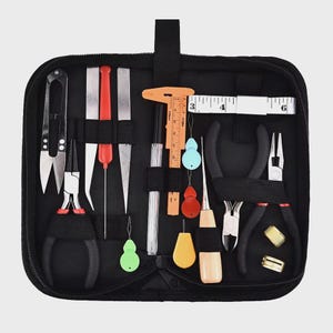 May include: A black zippered tool kit filled with various craft tools. Includes scissors, pliers, a ruler, a tape measure, and other small tools in red, orange, and silver. The kit is open, displaying the tools neatly arranged.