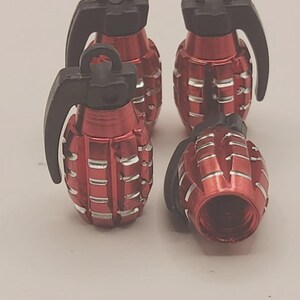 May include: Four red and black grenade-shaped objects. The objects have a textured, ridged design on the red body and a black lever and ring. The objects are arranged in a group, with one lying on its side.