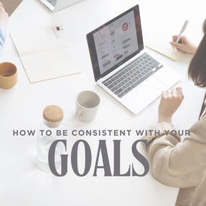 May include: A white table with two laptops, a notebook, and a mug. The text "HOW TO BE CONSISTENT WITH YOUR GOALS" is written in gray on the table. Below the text is the name "MONA-LEE BELIZAIRE" and the title "VISION COACH & STRATEGIST" in a light brown color.