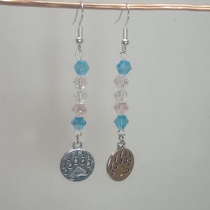 Op de afbeelding: Een paar oorhangers met een zilveren berenpootbedel. De oorhangers hebben een gradiënt van blauwe, roze en heldere kristallen kralen.