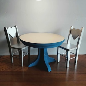 May include: A blue and white table set with two heart-shaped chairs. The table is round and has a white top with a blue rim. The chairs are made of wood and have a white heart-shaped back.