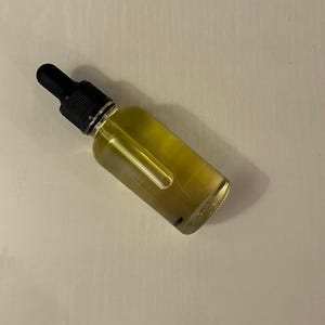 May include: A clear glass dropper bottle filled with a golden yellow liquid. The bottle features a black rubber bulb and a black plastic screw-top collar. The glass dropper tube is visible inside the bottle, extending into the yellow liquid.