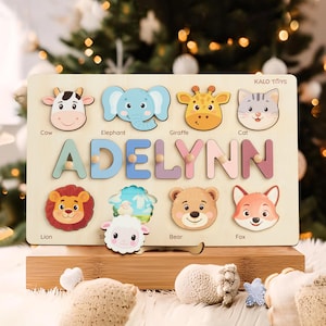 May include: Wooden name puzzle featuring the name "ADELYNN" in colorful letters. The puzzle includes animal-shaped pieces like a cow, elephant, giraffe, cat, lion, sheep, bear, and fox. The puzzle is on a wooden base.