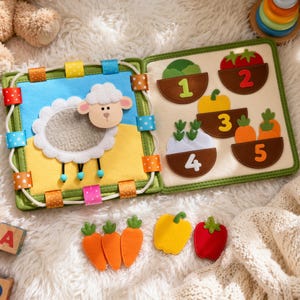 May include: A colorful felt activity book for toddlers. The open book displays a sheep scene and a counting page with vegetables. Includes felt carrots, a yellow pepper, and a red tomato. The book is designed with bright colors and soft textures.
