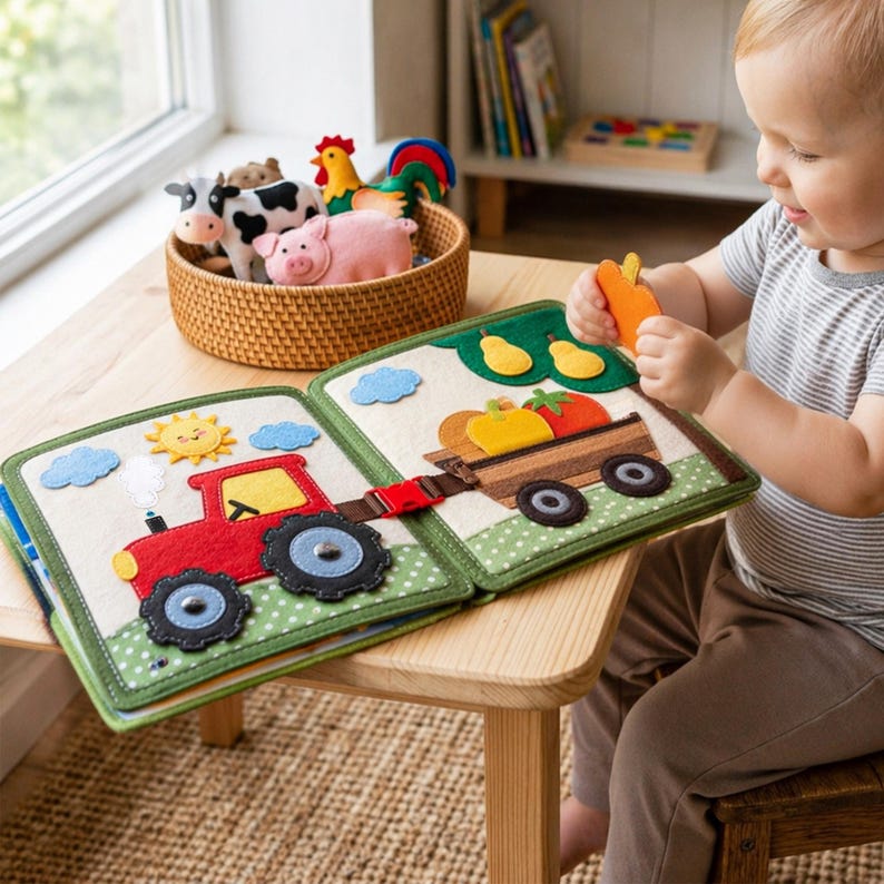 May include: A felt farm-themed activity book with a red tractor, a wagon filled with vegetables, and a basket of farm animals. The book is open on a wooden table, with a child holding a felt carrot.