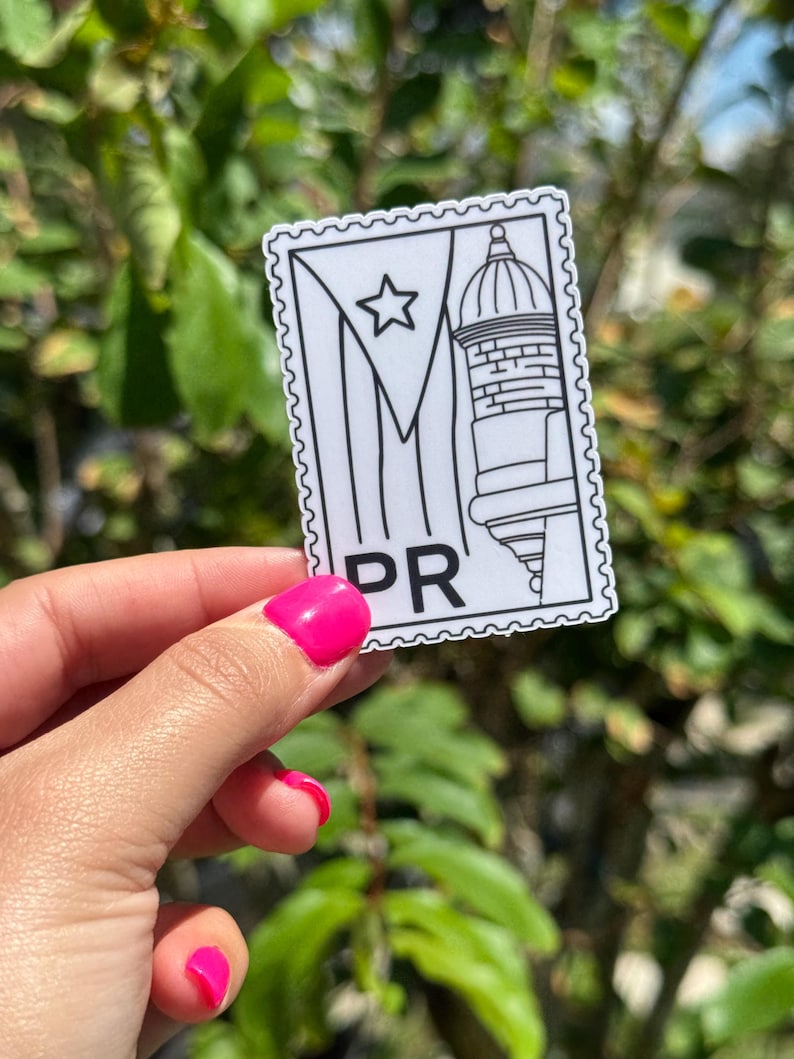 May include: A white and black sticker with a Puerto Rican flag design and the letters "PR". The sticker features a star, a building, and a flag design. The sticker is held in front of a green leafy background.