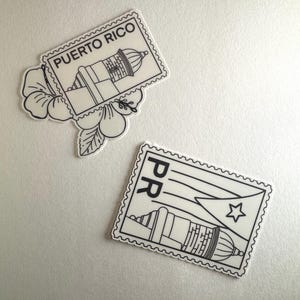 May include: Two white and black stickers with a Puerto Rico theme. One sticker is shaped like a postage stamp with the text "PUERTO RICO" and an image of a lighthouse. The other sticker has the Puerto Rican flag and a lighthouse.