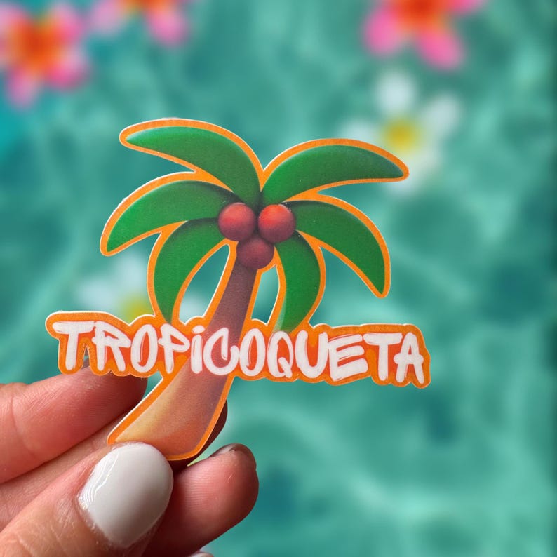 Op de afbeelding: Een kleurrijke sticker met een cartoon palmboom met groene bladeren, drie rode kokosnoten en een bruine stam. De sticker heeft het woord "TROPICOQUETA" in oranje letters. De achtergrond is een wazig turquoise.