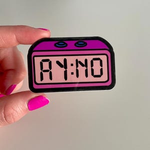 May include: A pink alarm clock sticker with a black digital display that reads "AY:NO".