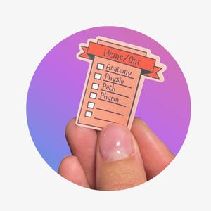 May include: A sticker with a peach-colored checklist design, featuring the text "Heme/Onc" at the top and a list of subjects including "Anatomy," "Physio," "Path," and "Pharm." The sticker is held against a gradient purple and blue background.