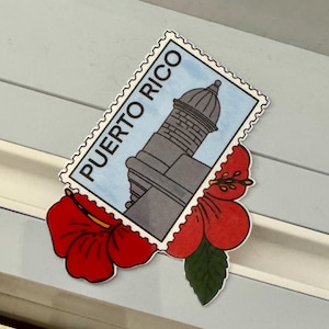 May include: A sticker featuring a gray lighthouse illustration on a blue background, labeled "PUERTO RICO" in white text. The sticker is adorned with a red hibiscus flower and green leaf.