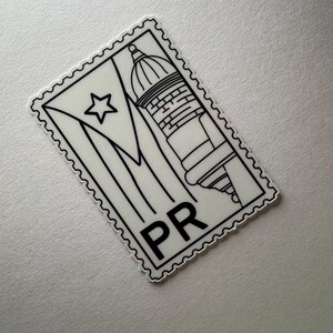 May include: A black and white sticker in the shape of a postage stamp. The sticker features the flag of Puerto Rico, a building, and the letters "PR". The sticker has a scalloped edge.