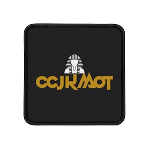 Puede incluir: Alfombrilla de ratón cuadrada negra con un gráfico dorado y blanco. El gráfico presenta una cabeza de faraón estilizada y el texto "CCJRMOT" en dorado. La alfombrilla tiene un borde negro.