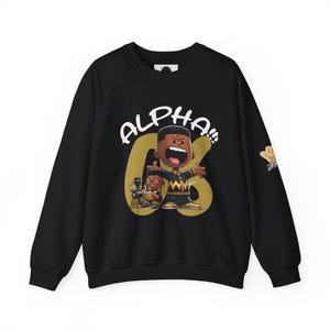 May include: Black sweatshirt with a gold and white graphic of a cartoon character with the text "ALPHA" on the front. The character is wearing a yellow and black striped shirt and a black hat. The sweatshirt has a gold and white graphic on the sleeve.