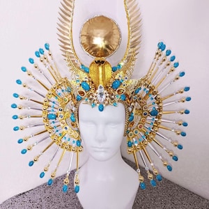 May include: A gold and silver headpiece with blue and gold beads. The headpiece has a large gold sun disc in the center and two wings on either side.