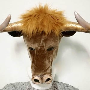 May include: A brown plush bull mask with gold horns. The mask has a furry brown face and a black nose.