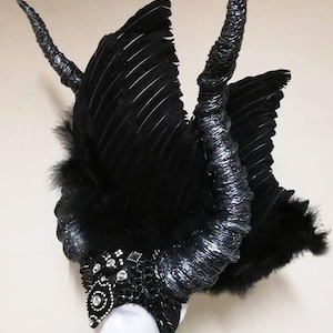 May include: A black feather headdress with silver horns and a jeweled crown. The headdress is made of feathers, wire, and beads.