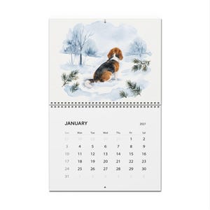 May include: A wall calendar for January 2027 featuring a watercolour illustration of a beagle dog sitting in a snowy landscape with pine branches and trees. The calendar grid displays the days of the month in black text on a white background.