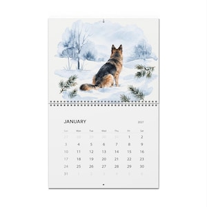 May include: A 2027 wall calendar for January featuring a watercolor illustration of a German Shepherd dog sitting in a snowy landscape with blue-toned trees and pine branches. The calendar grid displays the month name and dates clearly.