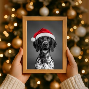 Può includere: Una stampa incorniciata raffigurante un cane in bianco e nero con un cappello di Babbo Natale rosso. Il cane sorride, con la lingua visibile. La cornice è in legno chiaro, lo sfondo è un albero di Natale sfocato.