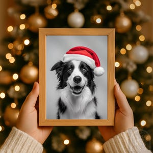 May include: A framed print featuring a black and white Border Collie wearing a red Santa hat. The dog is smiling with its tongue out. The print is held in a light brown wooden frame, with a blurred Christmas tree in the background.
