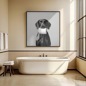 以下が含まれることがあります： 白い壁の前で、トイレットペーパーのロールを口にくわえた犬の白黒写真。写真は額縁に入っていて、バスルームの壁に飾られています。