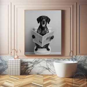May include: Monochrome framed print featuring a dog on a toilet, engrossed in a newspaper. The dog, with distinctive black and white markings, is the focal point. The print is set in a bathroom with a white tub and marble detailing.