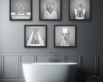 May include: Five framed black and white prints of cheetahs in a bathroom setting. One cheetah is in a bathtub, another in a robe, one on a toilet, one on a stack of toilet paper, and one with toilet paper on its head.