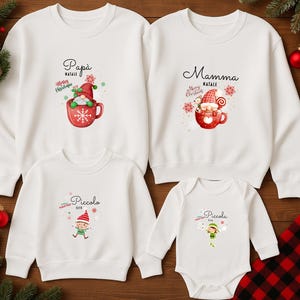 Könnte beinhalten: Weiße Sweatshirts und ein Body mit Weihnachtsmotiven. Die Sweatshirts zeigen "Papà" und "Mamma" mit Elfen-Illustrationen in Tassen. Der Body und ein Sweatshirt sagen "Piccolo Elf" mit einer Elfengrafik. Festliche Feiertagsbekleidung.