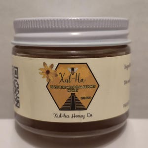 K&ouml;nnte beinhalten: Ein Glas Honig mit einem wei&szlig;en Deckel. Das Etikett ist gelb und zeigt eine Biene, eine Pyramide und den Text "Xul-Ha 100% Pure Melipona BeeCheii Honey Est. 2006 Xul-ha Honey Co."