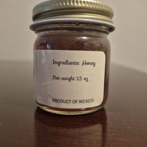 K&ouml;nnte beinhalten: Ein kleines Glas mit goldfarbenem Deckel, gef&uuml;llt mit Honig. Das Etikett lautet "Zutaten: Honig", "Nettogewicht 1,5 oz" und "Produkt aus Mexiko".