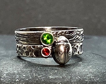 May include: A silver ring with three stones, a green stone, a red stone, and a silver ladybug charm.