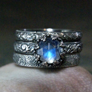 May include: A silver ring set with a large, round moonstone. The ring is made up of four bands, each with a different intricate design.