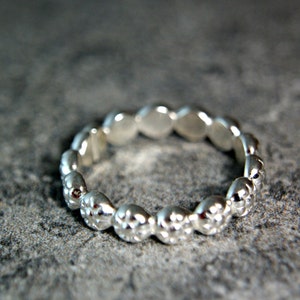 May include: A silver ring with a textured, beaded design. The ring is made of a series of small, rounded beads that are connected together to form a continuous band.