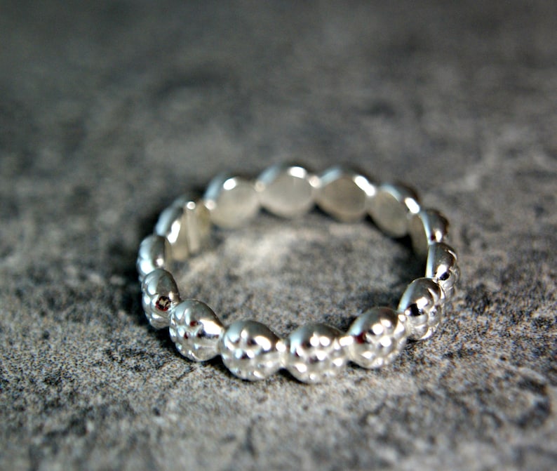 May include: A silver ring with a textured, beaded design. The ring is made of a series of small, rounded beads that are connected together to form a continuous band.