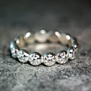 May include: A silver ring with a textured, beaded design. The ring is made of a smooth, polished metal and has a simple, elegant style.