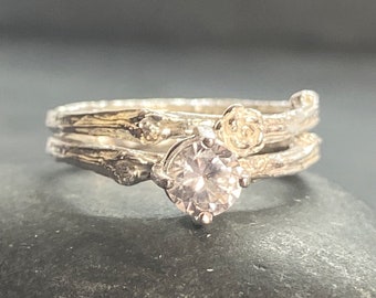 May include: A silver ring set with a clear round gemstone and two floral accents. The ring band is made of twisted silver wire.